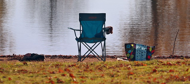 Single camping chair next to a lake with a bag close by
