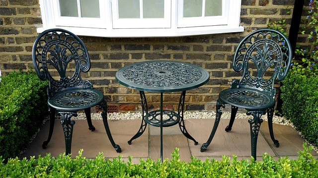 Two metal chairs and a metal table placed in the back garden on a small patio outside a window