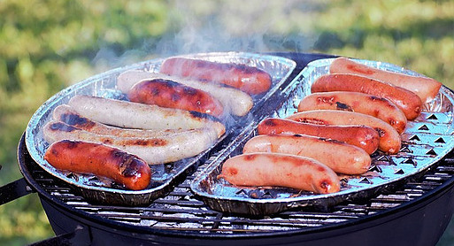 Tin foil plates full of sausages on a charcoal grill