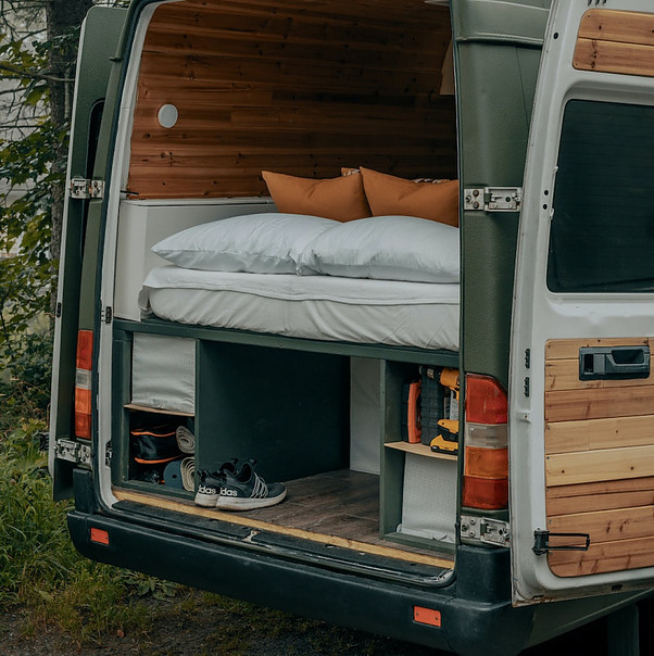 Picture of a campervan with its doors open revealing the bed and various items