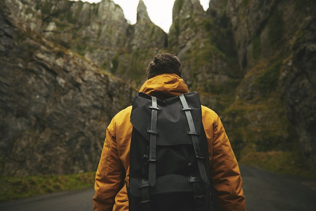 Guy wearing a backpack walking on a road through mountainous terrain