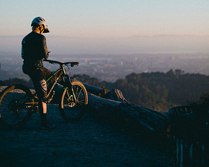 Guy sat on his mountain bike overlooking the city below whilst on his mobile phone