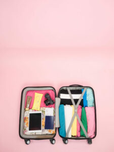 Open suitcase full of clothes on a pink background