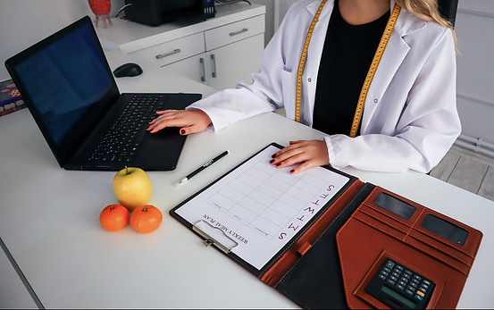Picture of a dietitian on her computer with an open exercise planner and two oranges and an apple in front of her