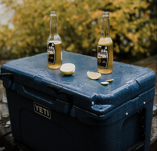 Two bottles of beer and a lemon sat on top of a cooler