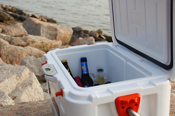 An open cooler full of drinks sat on a rock near the water