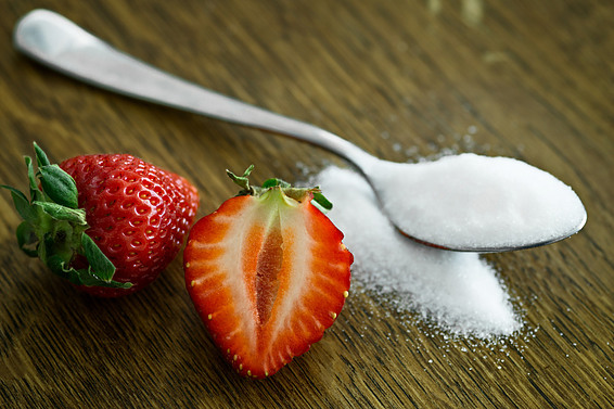 Picture of two strawberries next to a spoon of sugar