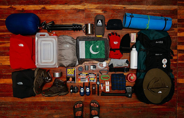 Picture of camping supplies placed on a wooden floor in front of a guy wearing sandals