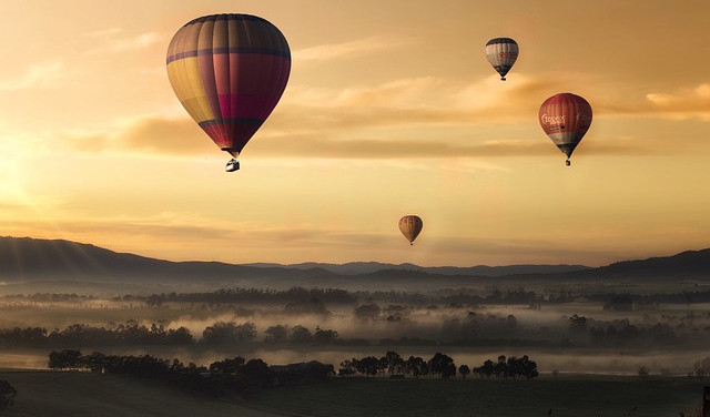 Four hot air balloons drifting through the sky on a misty morning below