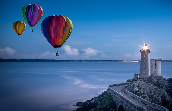 Picture of three hot air balloons flying over the water passed a lighthouse
