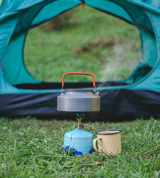 A kettle on a gas burner boiling outside a tent with a cup along side