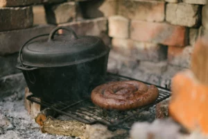 Picture of a Dutch oven and a large sausage cooking on an open grill