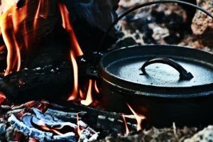 Picture of a Dutch oven half buried in a fire pit surrounded by flames
