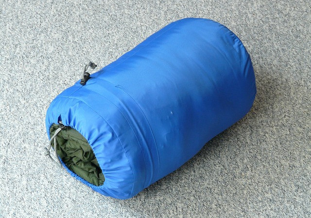 Green sleeping bag rolled up in its blue storage sack