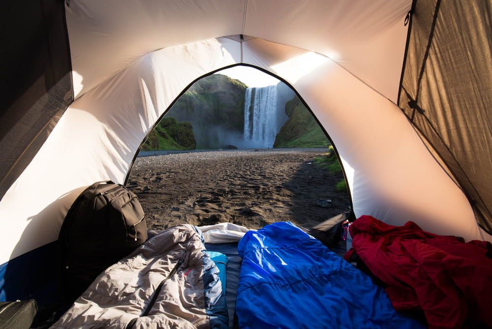 A view within a tent looking out onto a beautiful waterfall