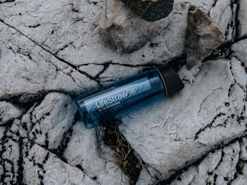 Blue water filter bottle with a black lid laying between rocks