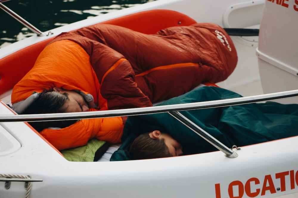 Father and son tucked up in their sleeping bags fast asleep in the front of their boat