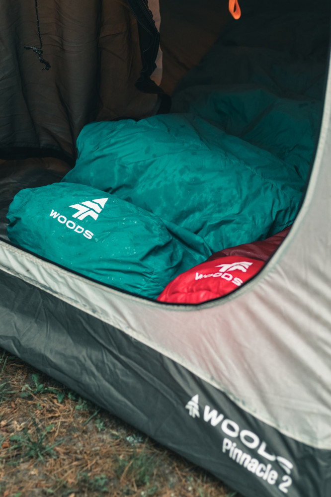 A wet green and red sleeping bag inside a tent with an open door pitched on the grass