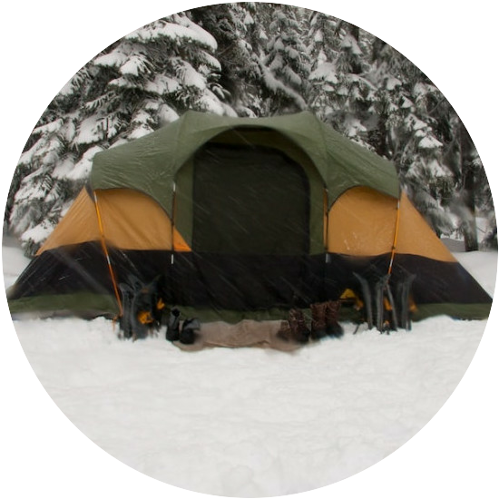 Green, orange and black tent pitched on snow surrounded by snow covered trees