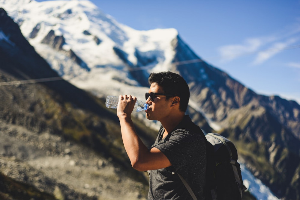 Hiker having a drink of water looking at his surroundings of snow capped mountains