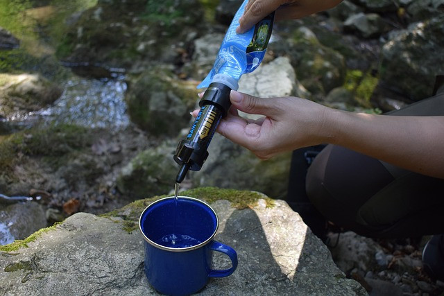 Hiker using a water filter to fill his blue cup that is placed on a rock
