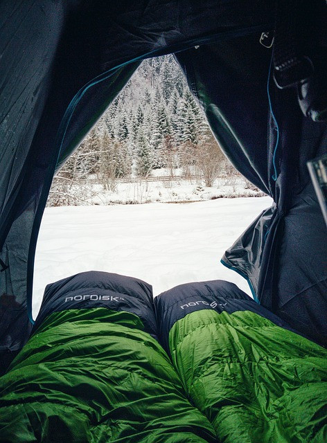 Two sleeping bags set up with an inside view looking out onto a very cold snowy day