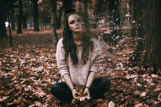 Woman sat in the woods on the ground amongst the leaves at one with nature