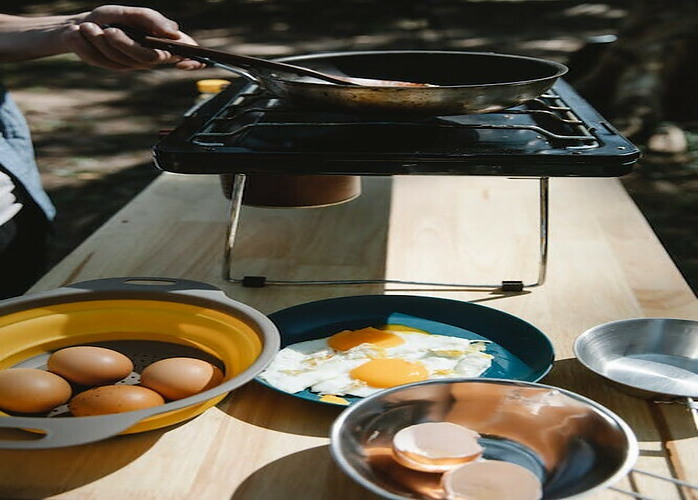 Bowls of unprepared food waiting the be cooked on a double burner camp stove placed on a table
