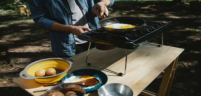 Fried eggs being cooked on a double burner camp stove placed on a table