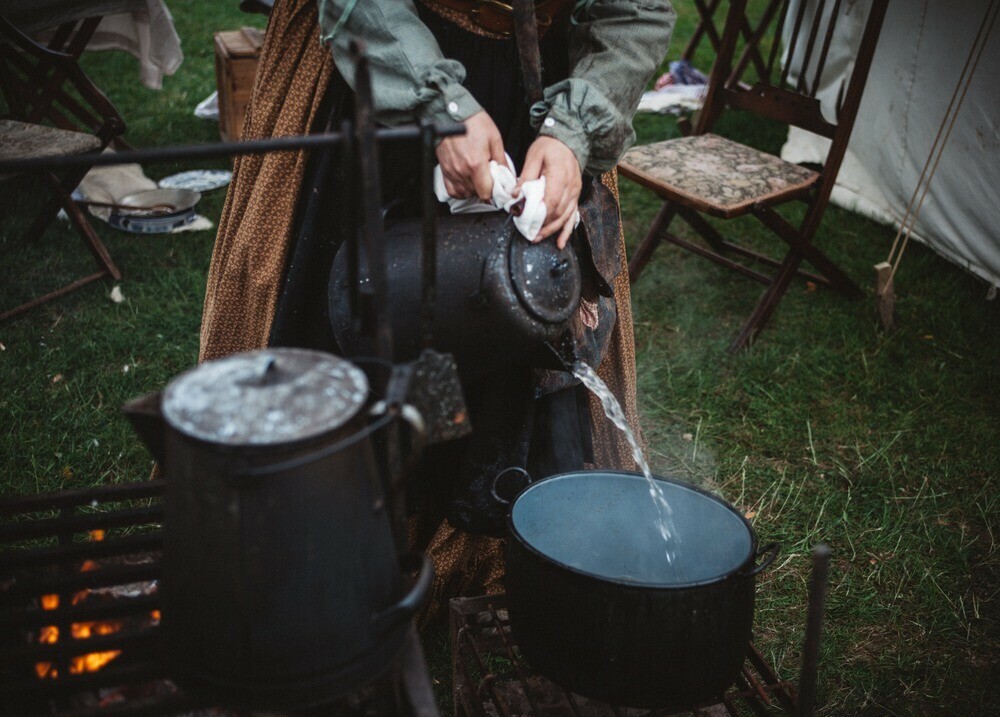 Boiling water being poured into a pot ready for cooking over an open firepit