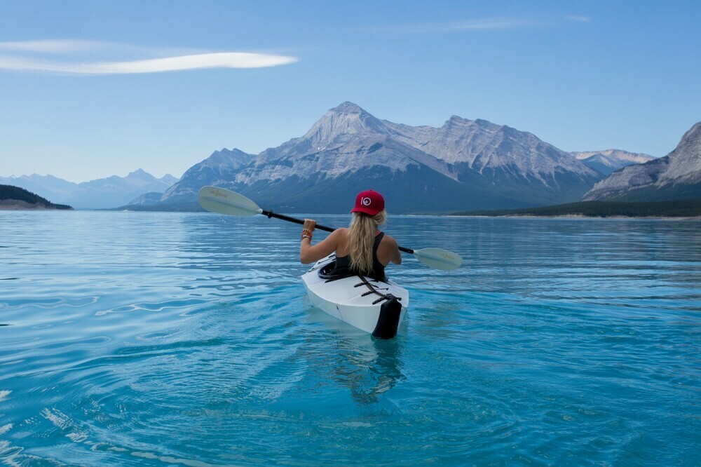 Individual kayaking on a lake with a view of snow peeked mountains in the distance