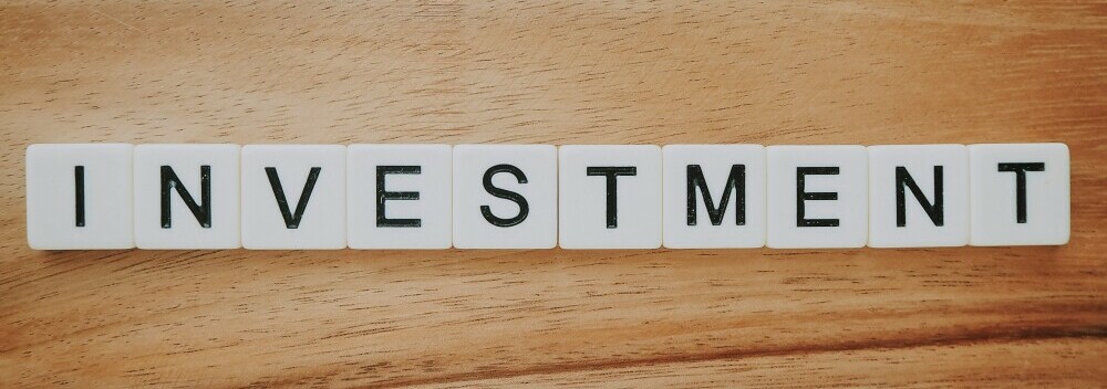 Scrabble pieces reading Investment laid on a wooden board