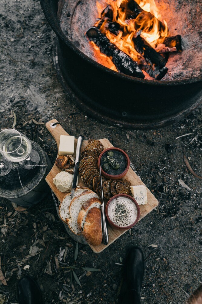 Selection of food on a cutting board placed near a cooking pot with burning  wood inside