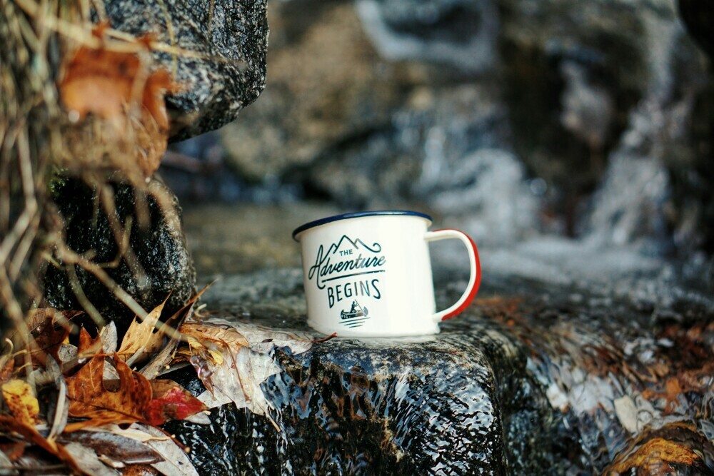 Tin cup on a rock reading "Adventure Begins"