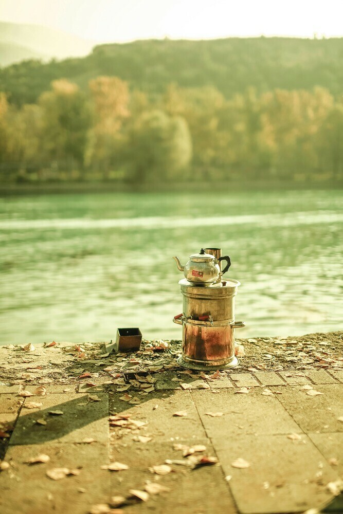 Two cooking pots with a kettle placed on top placed by the waters edge surrounded by trees