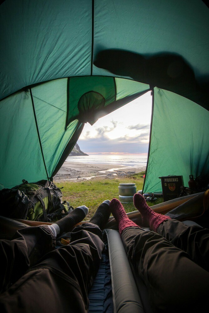 Two hikers relaxing in their tent looking out at the view, with their cooking pots placed at the tent entrance