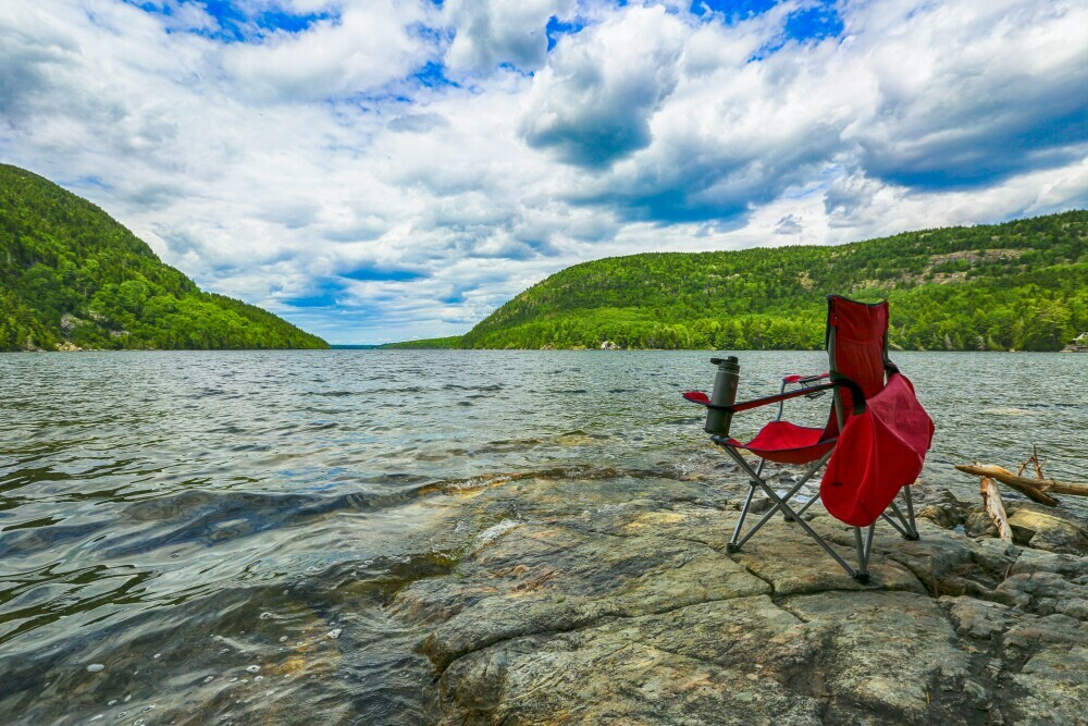 Camping chair placed on rocks by a lake with a view of the hills on a sunny day