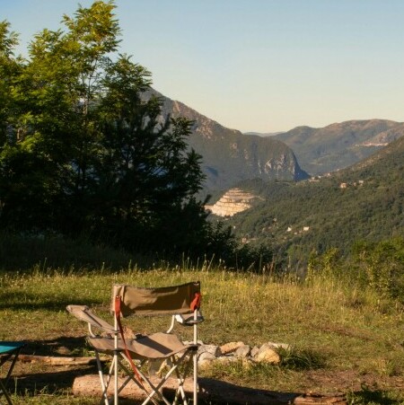 Four empty chairs on the grass with trees on the left and a view of the mountains
