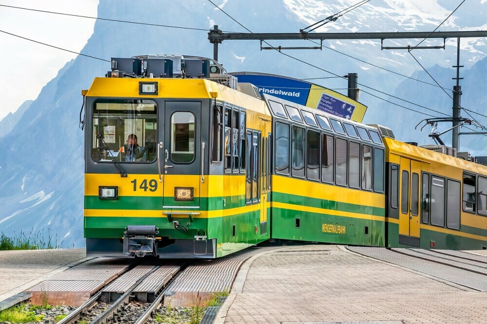 Image of a green, yellow and grey tram with a view of the mountains in the background