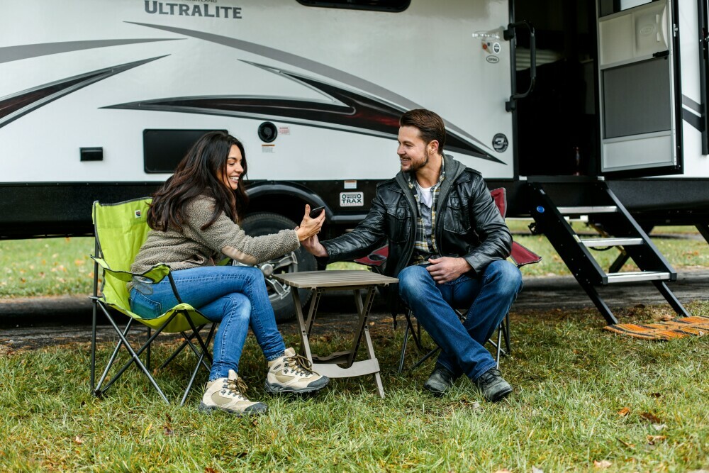 Two individuals sat outside their RV smiling and enjoying their day