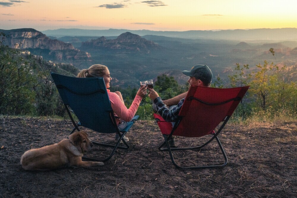 Two individuals sitting drinking wine enjoying the view with their dog laying behind them