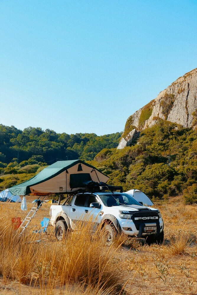 4X4 parked in a desert setting  with roof-top tent setup with bushes and rocky outcrop in the background