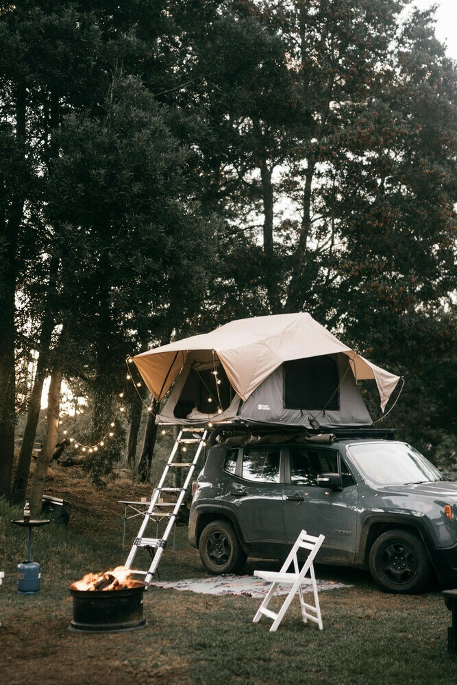 4X4 parked in a woodland with a roof-top setup with a firepit roaring below and a white chair close by
