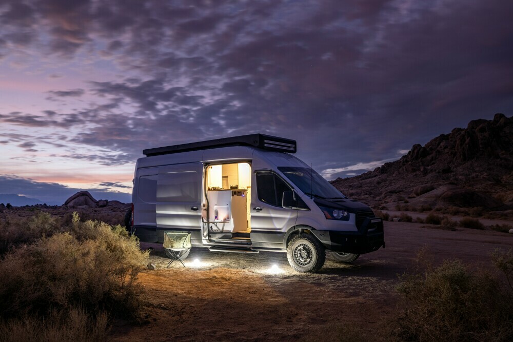 Converted camper parked on a hill-side with door open on a cloudy night