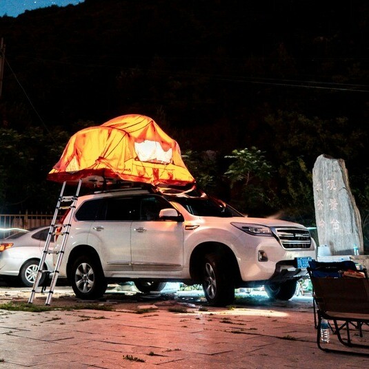 Vehicle in an industrial setting with a roof-top tent setup under a starlit sky